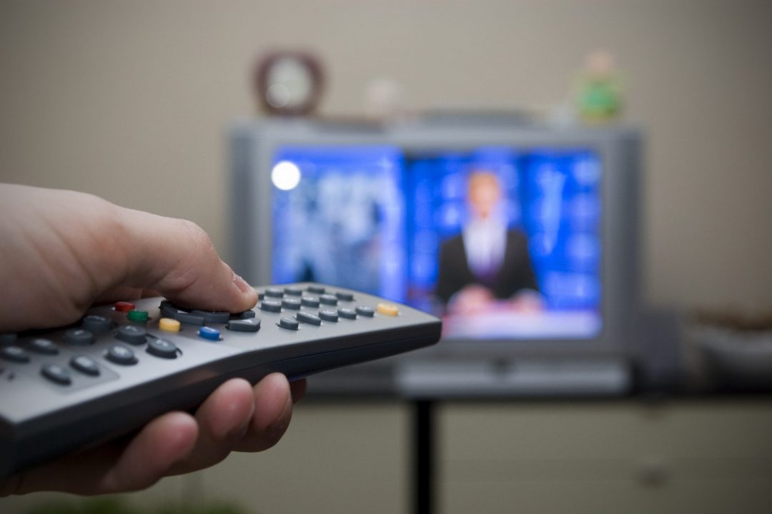 hand holding a remote control, tv in background